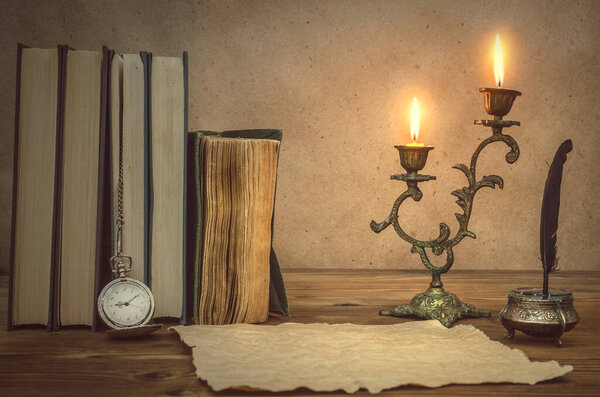 The old letter. Old books feather pen in inkpot, blank paper page sheet and retro pocket watch on retro wooden table background in the light of burning candle. Education. Back to school. Memoirs.
