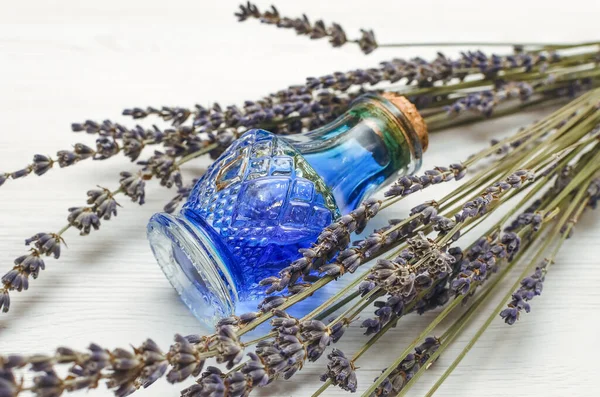 Dry lavender branches and bottle with blue medical tincture on white wooden background. Herbal medicine concept. Alternative medicine.