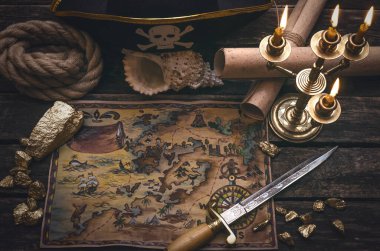 Korsan hazine haritası, altın külçeleri, hançer ve korsan şapkası eski ahşap masa arkasında. Deniz yolculuğu.