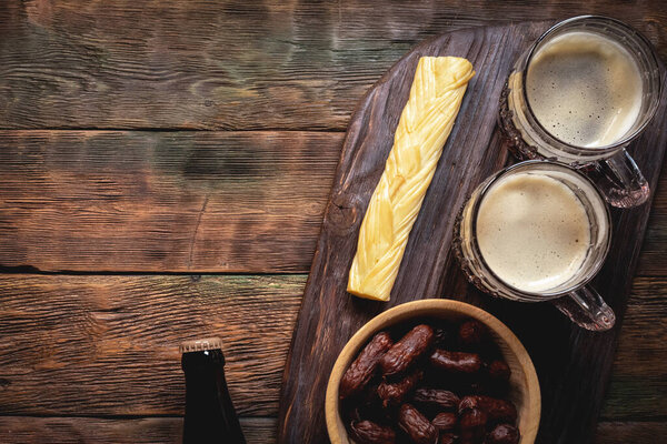Пивной стакан и закуски на фоне коричневого деревянного стола.