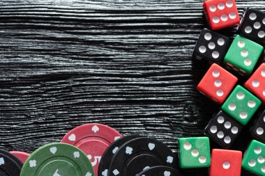 Siyah ahşap masa arkasında poker fişleri ve zarlar yığını.