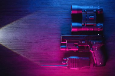 Casus Gizli Servis ajanı masa başı konsepti. Silah, radyo, dürbün ve el feneri fotokopi alanı ile neon arkaplanda..