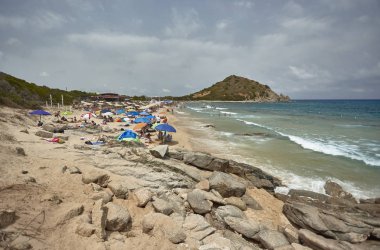 Güney Sardunya 'da denize bakan bir uçurum ve güneşli bir günde arka planda ufku kıran bir tepe olan bir banyoyla kurulmuş bir kumsal..