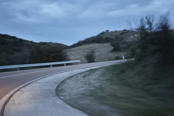 Road with a curve immediately forward traveled at high speed during twilight.