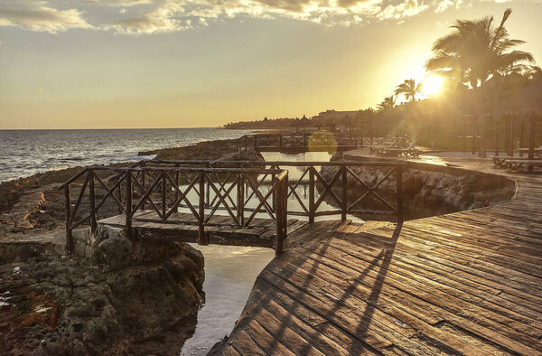 Sunset at sunset of a wooden pier set among the rocks on the coast of Puerto Aventuras in Mexico.