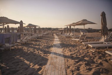 Güneş yatakları ve şemsiyeler gün batımında sahilde.