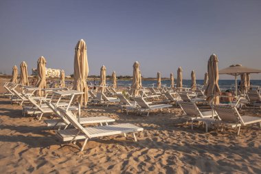 Gün batımında güneş yatakları ve şemsiyeler sahilde.