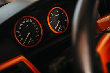 Aydınlatılmış araç gösterge paneli hız göstergesi ve turuncu aksanlı devir göstergesi, vurgulama hızı, motor performansı ve modern araç tasarımında otomotiv detayları
