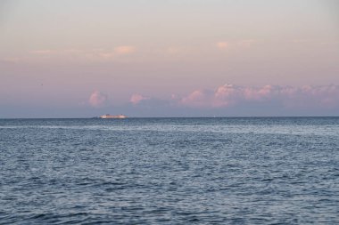 Gün batımında sakin mavi bir denizde seyreden bir yolcu gemisi, ufukta çarpıcı pembe ve mor bulutlarla çevrili, sottomarina, İtalya 'nın pitoresk ortamında yakalandı.