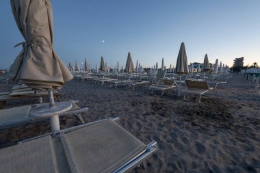 Kapalı plaj şemsiyeleri ve boş güneşlikler şafak vakti İtalya 'nın sottomarina kumsalında duruyor. Huzurlu ve huzurlu bir atmosfer yaratıyor.