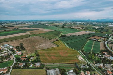 Po Vadisi 'nin tarımsal manzarasının hava görüntüsü, ekilmiş tarlaların sergilenmesi, dolambaçlı sulama kanalları, ve bulutlu bir gökyüzünün altında dağınık evler.