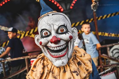 Roma, İtalya 10 Eylül 2025: Çocuklar bariyerin arkasından izlerken maskeli ve kostümlü korkunç bir palyaço perili bir evde tehditkar bir şekilde sırıtıyor.