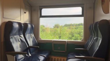 Roma, İtalya, 10 Eylül 2025: güneş ışığı bir tren vagonunda boş mavi koltukları aydınlatıyor, pencereden geçen yeşil tarlaları gösteriyor