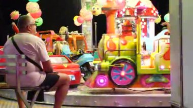 Roma, İtalya, 10 Eylül 2025: Gece vakti park operatörü tek başına oturuyor, renkli, aydınlık çocuk arabalarını akşam karanlığında boş duruyor.