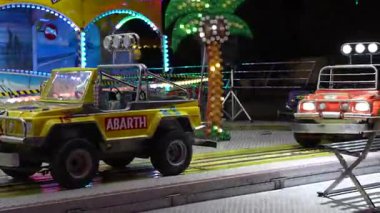 Roma, İtalya, 10 Eylül 2025: renkli oyuncak arabalar gece atlıkarıncada dönüyor, çocuklar tarafından bir lunaparkta sürülüyor, parlak ışıklar ve sponsor logoları var.
