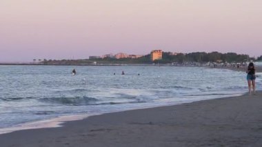 Sottomarina, İtalya 10 Eylül 2025: pembe ve mor gün batımı gökyüzü sottomarina plajı üzerinde, İtalya kıyılarında yürüyen genç bir kadınla birlikte