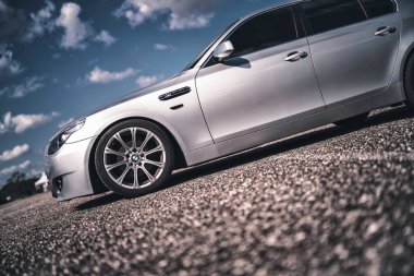 Milan, İtalya 20 Eylül 2025: Arkaplanda çarpıcı bulutlu bir gökyüzü ile dokulu çakıl yüzeyi üzerine park edilmiş parlak tasarım ve premium özelliklerini sergileyen gümüş renkli bmw sedan.