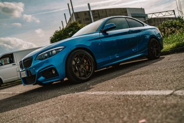 Milan, İtalya 20 Eylül 2025: asfalta park etmiş mavi BMW spor coupe, parlak metalik vücut ve dramatik bulutlu gökyüzü altında koyu renk özel yapım tekerlekler.