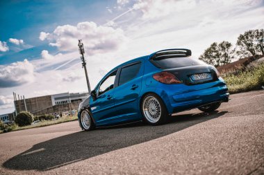 Milan, İtalya 20 Eylül 2025: Mavi peugeot 207 hatchback aşırı duruş: düşük süspansiyon, sonraki pazar tekerlekleri ve bulutlu gökyüzü altında arka spoiler