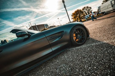 Milan, İtalya 20 Eylül 2025: Mercedes-amg üstü açık spor araba mat siyah kaplama ve turuncu fren kalibrelerini sergiliyor, asfaltta güneşli bir gökyüzü ve arka planda insanlar var.