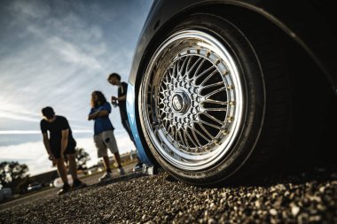 Milan, İtalya, 20 Eylül 2025: Bir grup arkadaş güneş batarken otomotiv yaşam tarzının tadını çıkarırken, krom kaplama ve altın rengi detaylarla özelleştirilmiş bir arabanın yanında sosyalleşiyorlar.