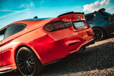 Milan, İtalya 20 Eylül 2025: çakıllı bir yolda duran kırmızı BMW spor coupe, parlak mavi gökyüzü altında parlak tasarımı ve güçlü duruşunu sergiliyor, arka planda başka bir araba var.