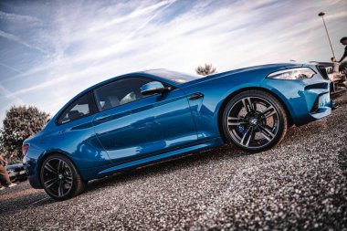 Milan, İtalya 20 Eylül 2025: Mavi BMW M2 spor spor coupe otoparkı açık hava otomobil buluşmasında bir çakıl yüzeyi üzerinde, parlak bir gökyüzü altında agresif tasarım ve performans özelliklerini vurguluyor