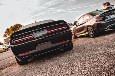 Milan, İtalya 20 Eylül 2025: Dodge Challenger ve BMW 2 'yi canlı bir arabada park etmiş, gün batımında buluşuyor, çift BMW' ye yaslanıyor, performans kültürü sergiliyor.