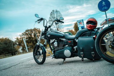 Milan, İtalya 20 Eylül 2025: Harley-Davidson motosikleti yol kenarına park edilmiş turuncu bir miğferle arka planda bir benzin istasyonu bekliyor.