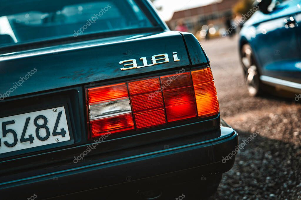 Milan, italy 20 september 2025: bmw e30 318i vintage automobile showing its rear end, taillight, and emblem while parked on a gravel surface outdoors during a sunny day