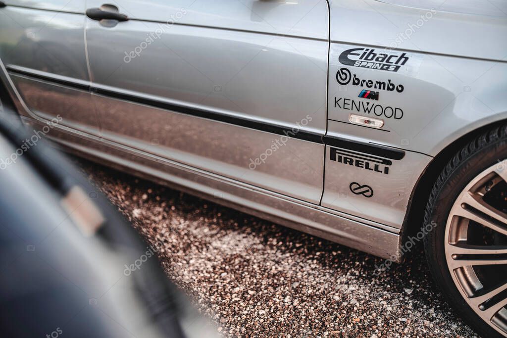 Milan, italy 20 september 2025: bmw sports car side panel with sponsor decals and logos on silver body, parked on gravel, showing tuning details