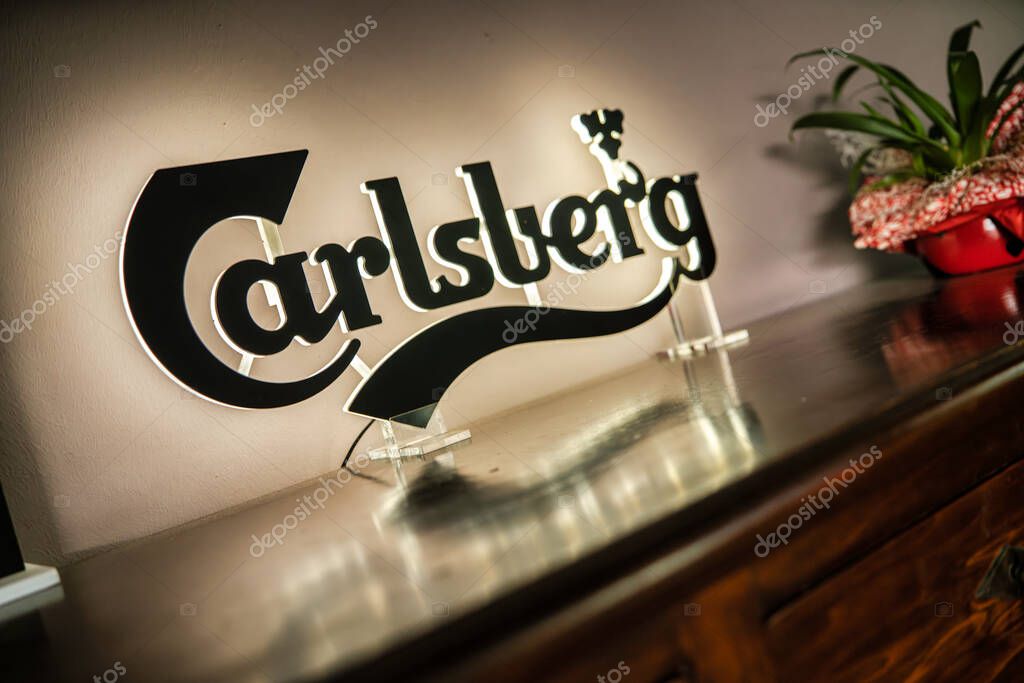 Milan, italy 20 september 2025: carlsberg branding illuminates a modern sign standing on a polished wooden bar, reflecting soft light and creating a casual ambiance for relaxation