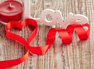 Beyaz aşk işareti ve mum ile ahşap arka plan üzerinde kırmızı kıvrılmış kurdele