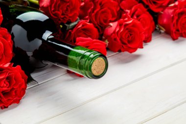 Beyaz ahşap arka plan üzerinde kırmızı gül ve şarap şişesi tomurcukları