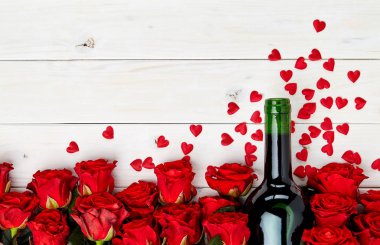 Konfeti ile beyaz ahşap arka plan üzerinde kırmızı gül ve şarap şişesi tomurcukları