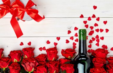 Konfeti ve hediye ile beyaz ahşap arka plan üzerinde kırmızı gül ve şarap şişesi tomurcukları