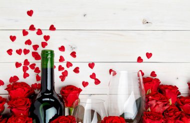 Konfeti ve cam ile beyaz ahşap arka plan üzerinde kırmızı gül ve şarap şişesi tomurcukları