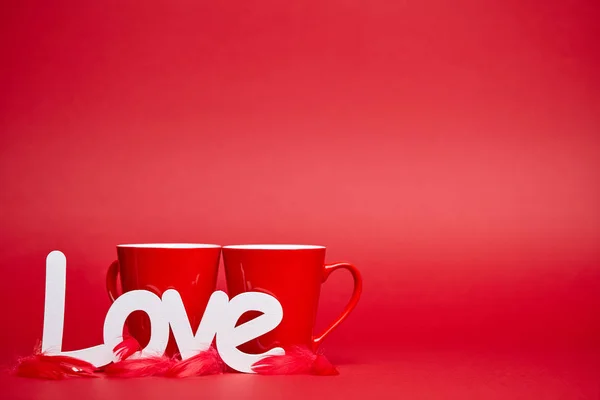 Roter Hintergrund Mit Zwei Tassen Weißem Liebeszeichen Und Federn — Stockfoto