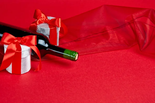 İki hediye ve şarap şişesi ile kırmızı arka plan