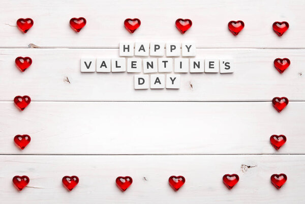 Texture of red heart figures shaped into frame with phrase inside, on white wooden background 