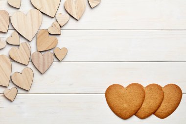 Beyaz ahşap arka plan üzerinde farklı boyutta kalp figürleri ve zencefilli çörekler 