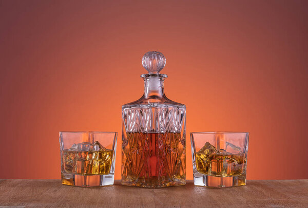 Старомодный стакан и графин с алкоголем, виски напиток на теплом, темно-оранжевом фоне и дерево
