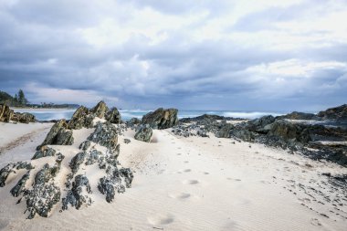 Kum mavi bulutlu gökyüzü altında kayalık Beach üzerinde ayak izleri 