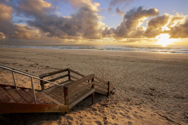 Wooden stairs on sandy beach during sunset in cloudy sky