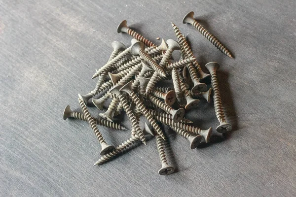 Beyaz bir yüzeye saçılmış alçıpan vidalarının yakın plan çekimi. Kendi kendine dokunan vidalar açık ve koyu gri karışımından oluşur. Dokularını ve şekillerini vurgularlar.