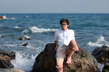 Genç Asyalı adam deniz kıyısı kayada rahatlatıcı. Yaz tatil kavramı.