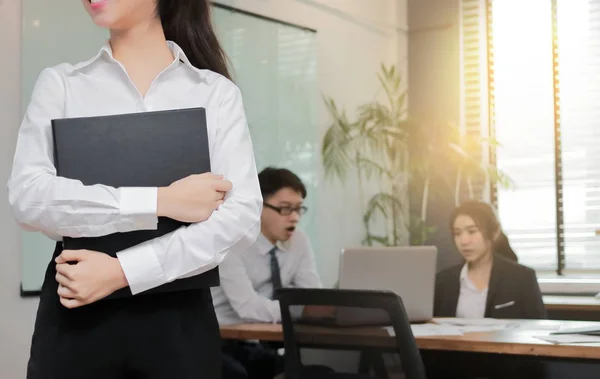 Leadership young Asian business woman with document folder standing against her colleague in office background.