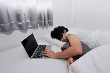 Yorgun overworked Asya adam yatakta uyuyan dizüstü bilgisayar ile.