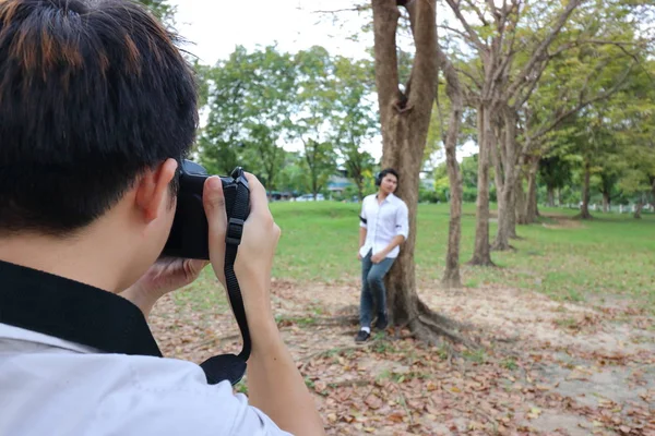 Back view of photographer taking a photo of young man in summer park.