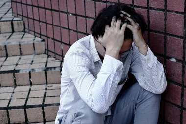 Yüzünü elleriyle kapsayan karışık anksiyete genç Asya iş adamı arka görünümü.